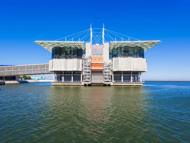 a large building on the water with a blue sky Lisbon Oceanarium